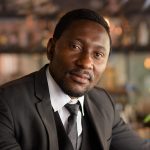 Portrait of handsome bearded African businessman in suit relaxing at the coffee shop