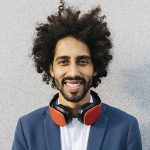 Portrait of smiling young businessman with headphones at a wall
